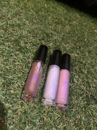 three bottles of lip gloss sitting on grass