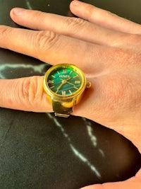 a woman's hand holding a gold watch ring