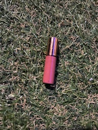 a pink lipstick laying on the grass