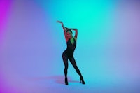 a woman in a black outfit is dancing in front of a neon light