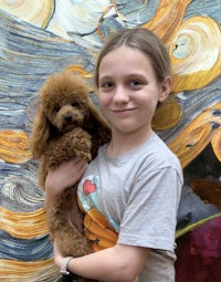 a young girl holding a poodle in front of a painting