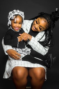 a woman and her daughter are sitting on a chair with a black background