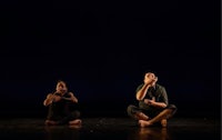 two dancers sitting on the floor in front of a dark stage