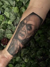 a black and grey tattoo of a demon on a person's forearm