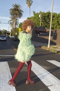 a woman in a green furry coat crossing a street