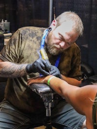 a man tattooing a woman's arm at a convention
