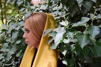 a woman wearing a yellow scarf in front of a bush