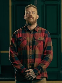 a bearded man in a plaid shirt standing in a dark room
