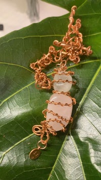 a rose quartz and copper wire necklace on a leaf