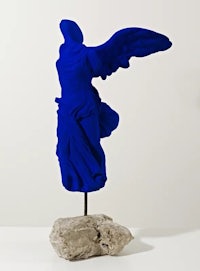 a blue sculpture of an angel on a rock