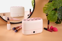 a pink and white makeup organizer on a table next to a mirror