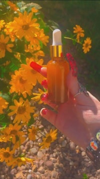 a hand holding a bottle of oil in front of yellow flowers