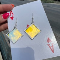 a person holding up a pair of mirrored square earrings