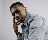 a black man in a denim jacket posing with his hand on his chin