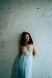 a woman in a blue dress leaning against a brick wall
