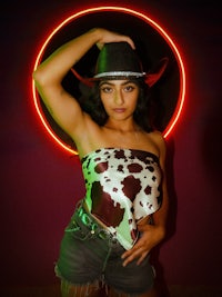 a woman in a cowboy hat posing in front of a neon light