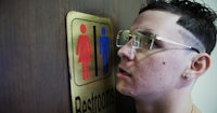 a man wearing glasses is standing in front of a restroom sign