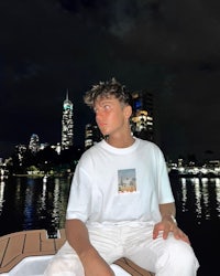 a man sitting on a boat at night wearing a white t - shirt