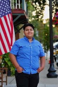 a young man in a blue shirt standing in front of an american flag