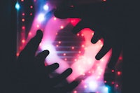 a silhouette of two hands reaching for a glowing light