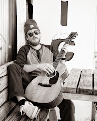a man sitting on a bench holding an acoustic guitar