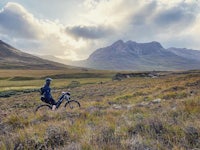 a person riding a mountain bike through a grassy field with mountains in the background