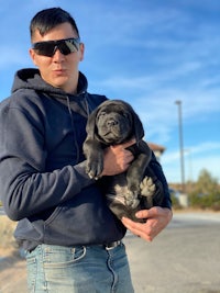 a man in sunglasses holding a black puppy