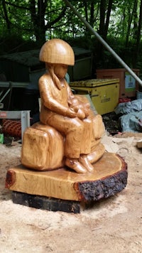 a wooden sculpture of a boy sitting on a log