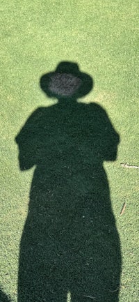 the shadow of a person in a hat on the grass