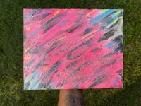 a person holding up a pink and blue painting on grass