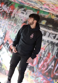 a man in a black hoodie standing in front of graffiti
