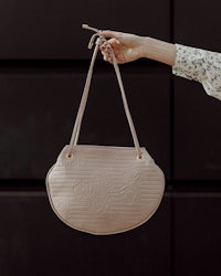a woman is holding a handbag in front of a black wall