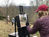 a woman painting on an easel in a field