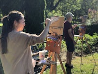 a woman is painting on an easel in a garden