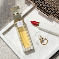 a bottle of perfume and a red lipstick on a marble tray