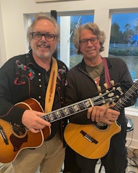 two men standing next to each other holding guitars