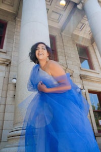 a woman in a blue tulle dress posing in front of pillars