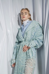 a woman in a blue coat posing in front of a curtain