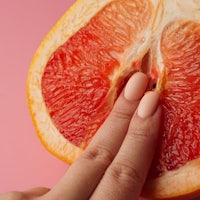 a woman's hand holding a grapefruit on a pink background
