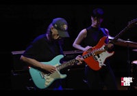 two people playing guitars on stage