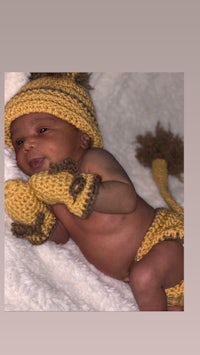a baby in a yellow knitted outfit laying on a blanket