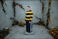 a man in a yellow and black striped sweater standing in a room with flowers