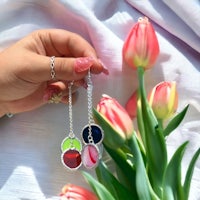 a person holding a pair of earrings with tulips in the background