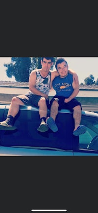 two men sitting on top of a car