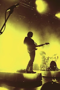 a man playing guitar on stage in front of a yellow light