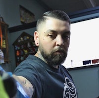 a man with a beard taking a selfie in a tattoo shop