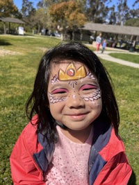 a little girl with face paint sitting on the grass