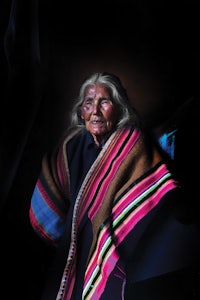 a woman in a colorful blanket sitting in front of a dark background