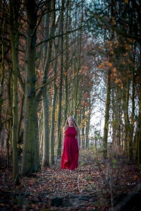 a girl in a red dress walking through the woods
