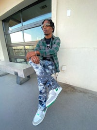 a man sitting on a bench wearing a camouflage shirt and sneakers